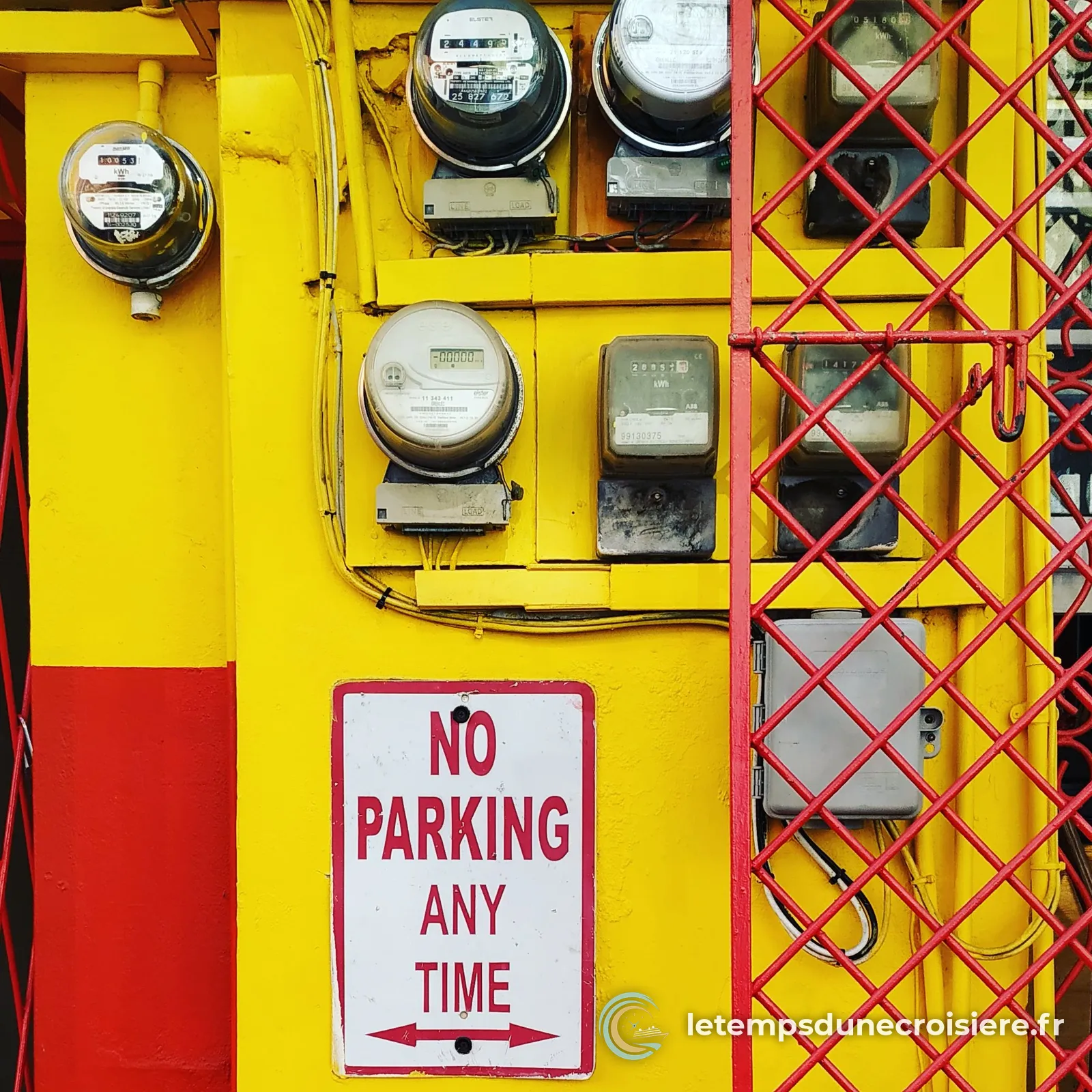 Compteurs électriques et panneau No parking any time sur un mur jaune et rouge