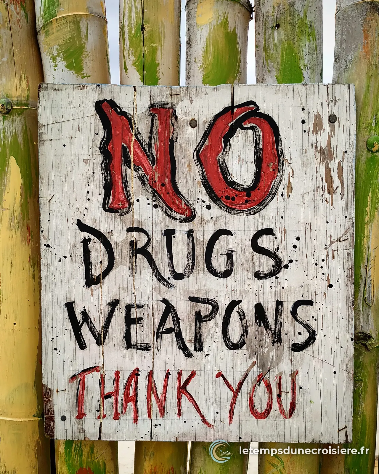 Panneau peint à la main No drugs, weapons, thank you, sur une palissade de bambou